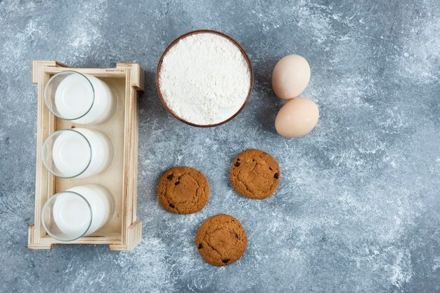 Tres vasos de leche con harina y huevos sobre una mesa gris.