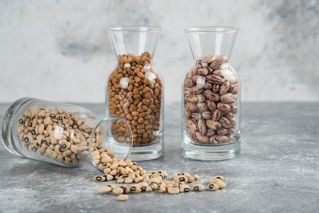 Tres vasos de tarro con frijoles sin preparar sobre una mesa gris.