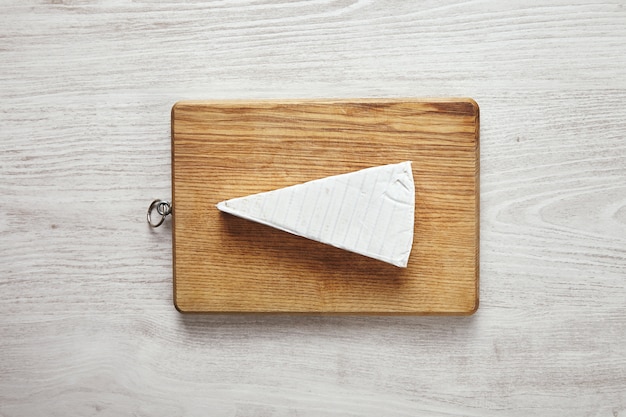Triángulo blanco fresco de sabroso queso brie en tabla de cortar aislado en blanco mesa de madera envejecida en el centro. Listo para comer, desayuno de servir. Concepto de presentación