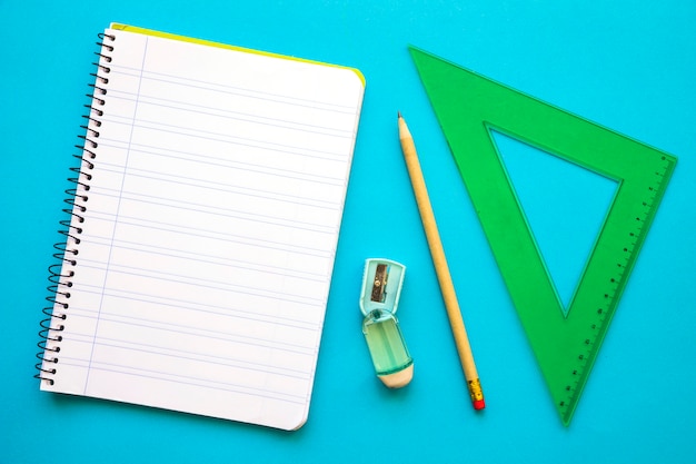 Triángulo y cuaderno cerca de lápiz y sacapuntas
