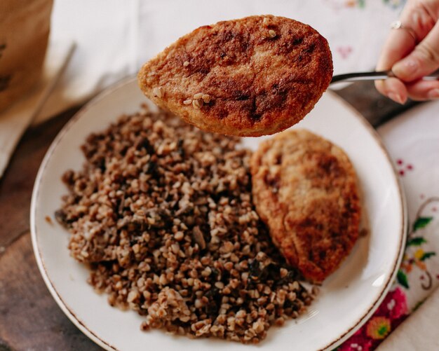 trigo sarraceno cocido junto con rebanadas de carne frita dentro de panes de pan de plato blanco en una mesa de pañuelos coloridos durante el día