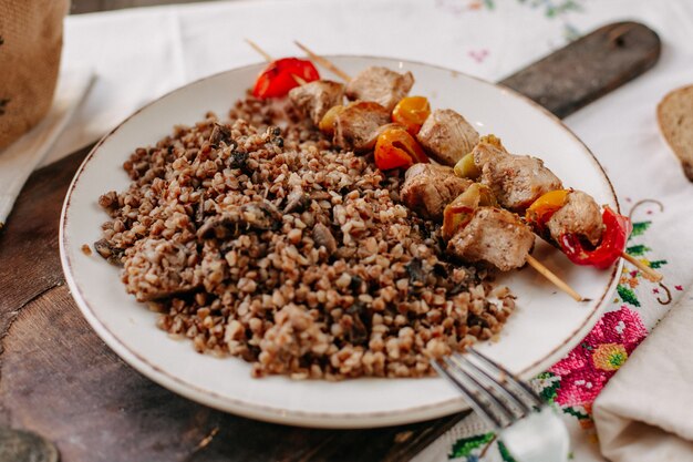 trigo sarraceno cocido junto con rebanadas de carne frita en palitos dentro de panes de pan de plato blanco en una mesa de pañuelos coloridos durante el día