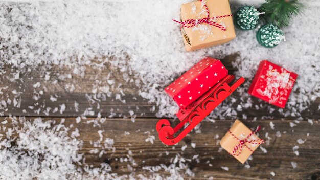 Trineo de juguete cerca de cajas presentes entre copos de nieve.