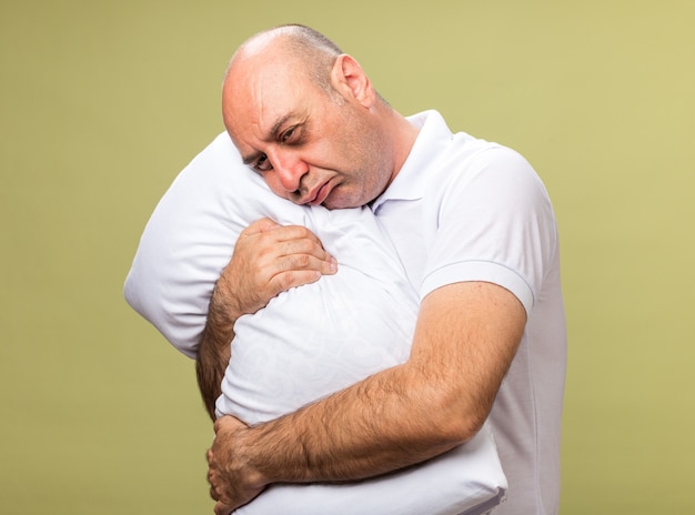 Triste adulto enfermo hombre caucásico sosteniendo y poniendo la cabeza sobre la almohada aislado en la pared verde oliva con espacio de copia