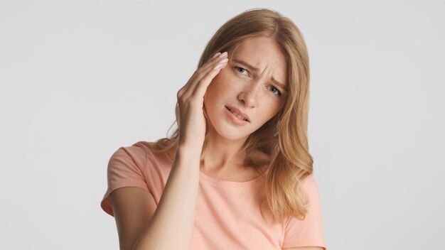 Triste chica rubia mantenga la mano en la sien sintiendo dolor de cabeza sobre fondo blanco Mueca de migraña