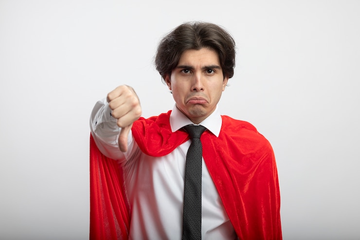 Foto gratuito triste chico joven superhéroe mirando a la cámara con corbata mostrando el pulgar hacia abajo aislado sobre fondo blanco.