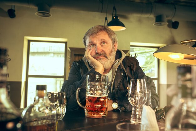 El triste hombre barbudo senior bebiendo cerveza en el pub