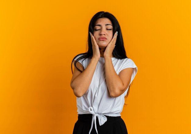 Triste joven caucásica pone las manos en la cara de pie con los ojos cerrados