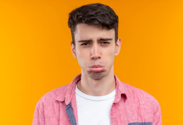 Triste joven caucásico vistiendo camisa rosa sobre fondo naranja aislado