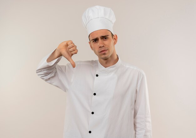 Triste joven cocinero vistiendo uniforme de chef con el pulgar hacia abajo con espacio de copia