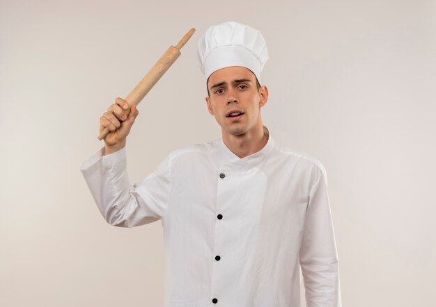 Triste joven cocinero vistiendo uniforme de chef sosteniendo un rodillo alrededor del hombro