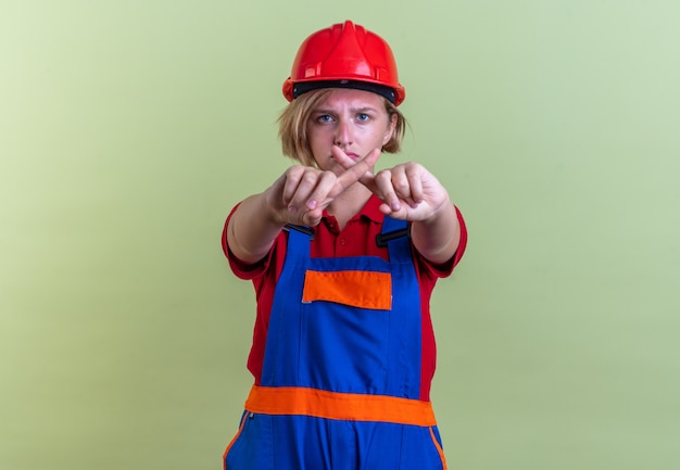 Foto gratuita triste joven constructor mujer en uniforme mostrando gesto de no aislado en la pared verde oliva