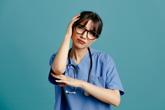 triste joven doctora vistiendo uniforme fith estetoscopio aislado sobre fondo azul.