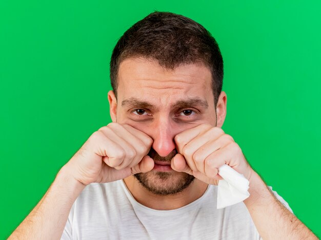 Triste joven enfermo secándose los ojos con los puños aislados en verde