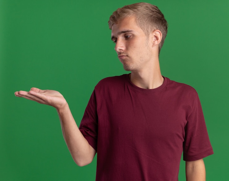 Foto gratuito triste joven guapo con camisa roja fingiendo sostener algo aislado en la pared verde con espacio de copia