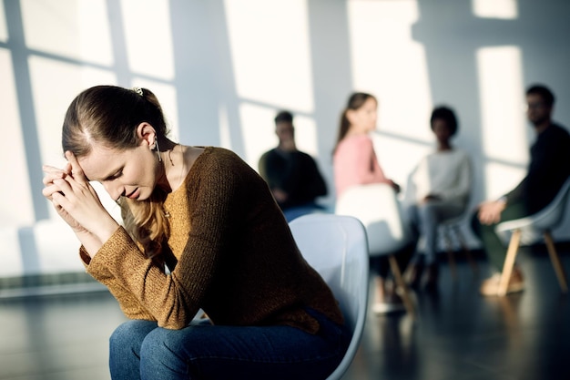 Triste joven mujer sentada aparte de los asistentes a la terapia de grupo en el centro comunitario
