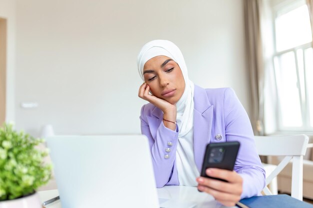 Triste joven musulmana usando teléfono móvil y computadora portátil