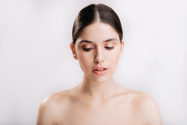 Triste joven con la piel limpia sin maquillaje en la cara posa para el retrato en la pared aislada.