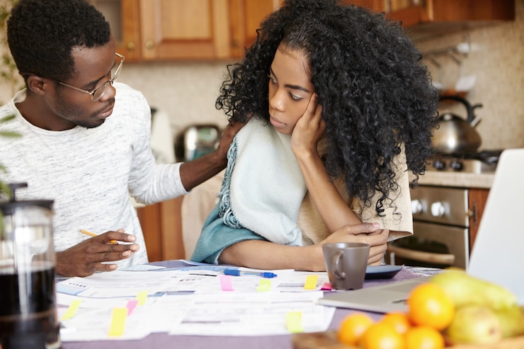 Foto gratuito triste mujer africana con peinado afro que parece triste e infeliz debido a problemas financieros en su familia mientras su esposo sentado a su lado, tocándole el hombro, tratando de animarla