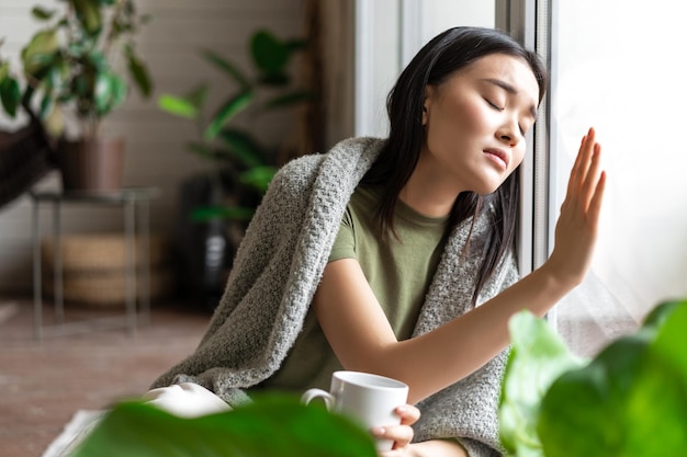 Triste mujer asiática desconsolada tocando la ventana de cristal y sintiéndose enfermo anhelando algo que se quede en ...