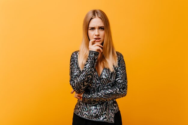 Triste mujer atractiva en chaqueta brillante posando en el estudio. Hermosa mujer ciega trastornada de pie en naranja.