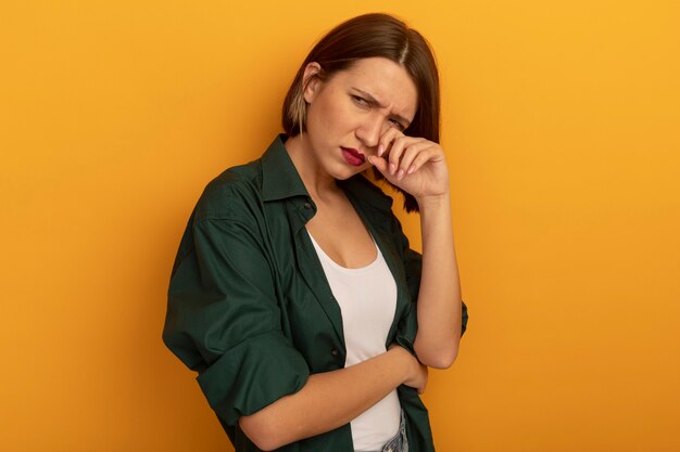 Triste mujer bastante caucásica pone el dedo en el párpado mirando de lado en naranja