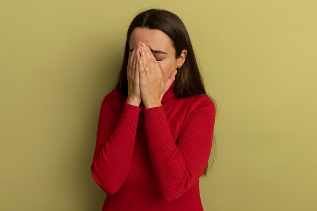 Triste mujer bonita caucásica con las manos en la cara en verde oliva