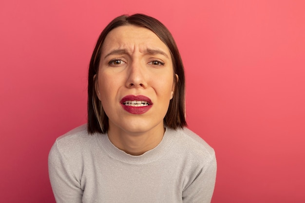 Triste mujer bonita mira al frente aislado en la pared rosa