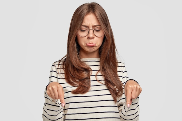 Triste mujer joven con gafas posando contra la pared blanca