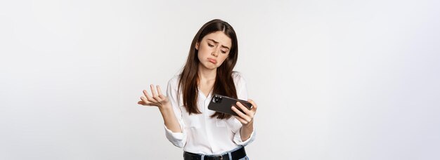 Triste mujer perdiendo en un videojuego móvil que se ve molesta y decepcionada por el teléfono inteligente que se enfurruña de pie