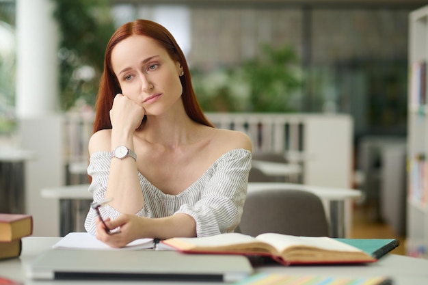 Triste mujer sentada a la mesa con libros