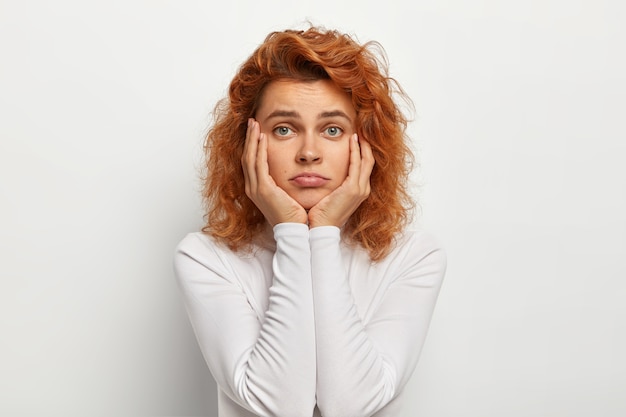 Foto gratuita triste mujer solitaria con cabello ondulado astuto, toca las mejillas