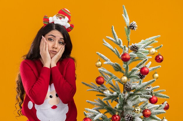 Triste niña bonita vistiendo suéter y diadema de santa claus