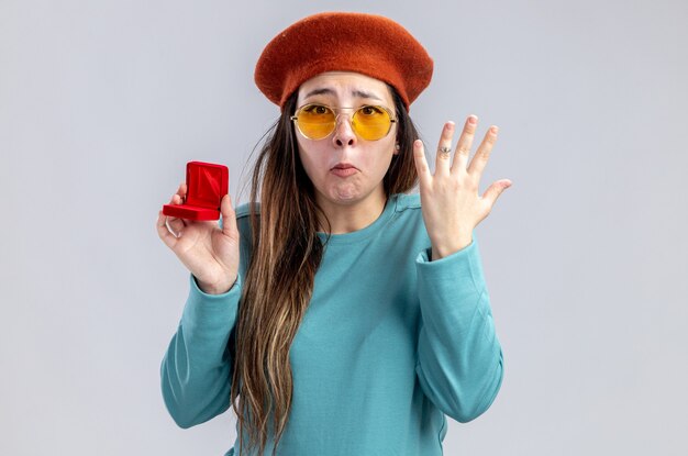 Triste niña en el día de San Valentín con sombrero con gafas lleva anillo de bodas aislado sobre fondo blanco.