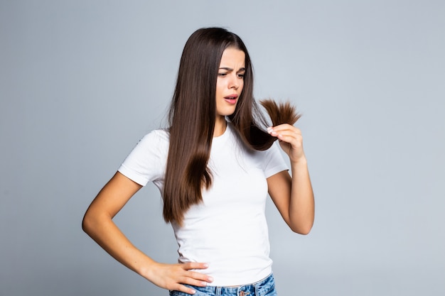 Triste niña mirando su cabello dañado aislado en blanco