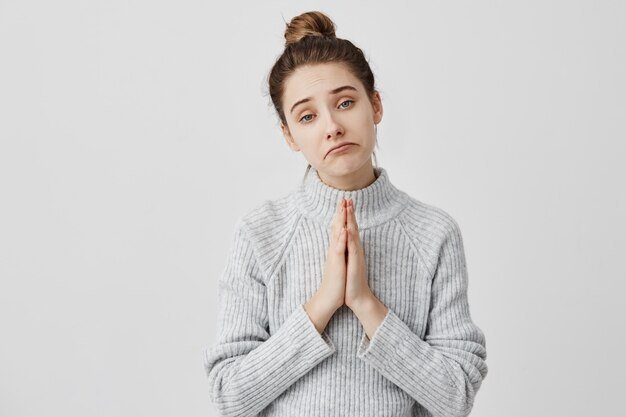 Tristes expresiones faciales de bella dama con las manos juntas para suplicar. Joven mujer está de moda suplicando a los padres por dinero. Lenguaje corporal