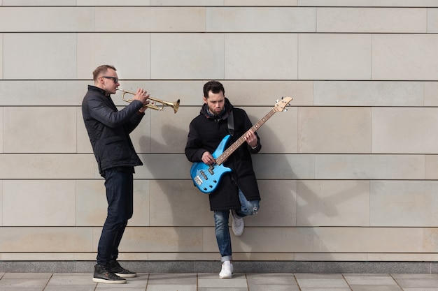 Trompetista y guitarrista tocando en frente de un muro