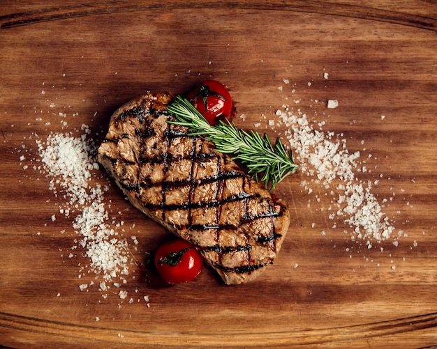 Trozo de bistec y tomates bien fritos sobre una tabla de madera