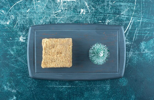 Un trozo de pastel sabroso con un pequeño árbol de Navidad en un plato oscuro. Foto de alta calidad