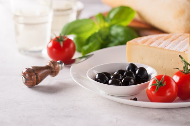 Trozo de queso en un plato con aceitunas y tomates