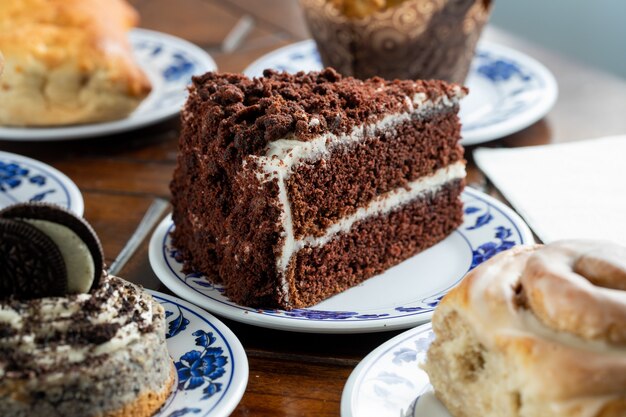 Trozo en rodajas de un delicioso pastel de chocolate en un plato azul-blanco rodeado de otros dulces