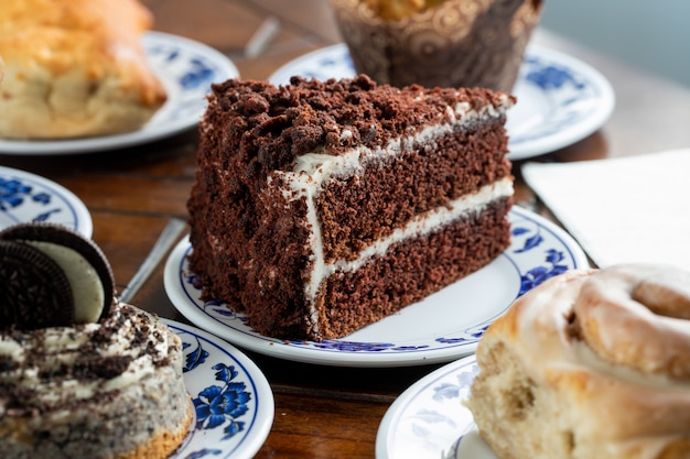 Trozo en rodajas de un delicioso pastel de chocolate en un plato azul-blanco rodeado de otros dulces