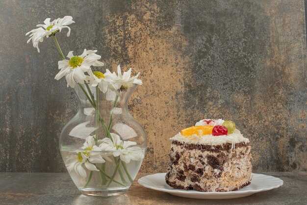 Un trozo de tarta de chocolate con bouquet de manzanilla sobre superficie de mármol.