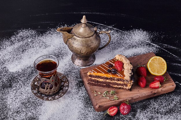 Un trozo de tarta de chocolate decorado con frutas sobre fondo oscuro con juego de té clásico.