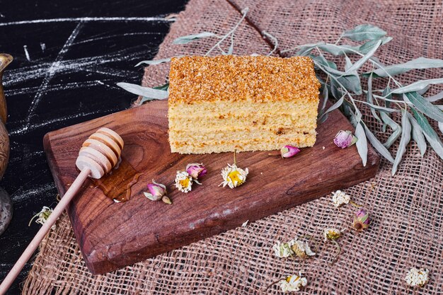 Un trozo de tarta de miel casera con flores secas y cuchara de miel sobre un mantel de lana.