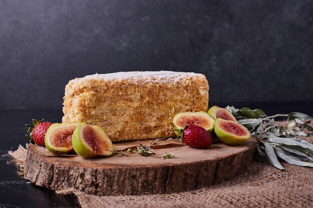 Un trozo de tarta de napoelon sobre fondo oscuro con higos y fresas.