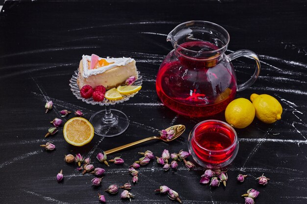 Un trozo de tarta de queso, limones y té negro sobre la mesa de mármol oscuro.