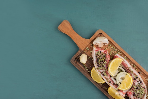 Trozos de carne cruda sobre tabla de madera con rodajas de limón.