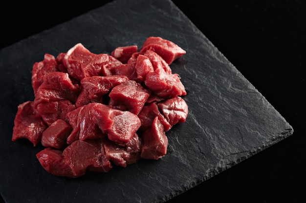 Trozos de carne fresca cruda aislado en el tablero de piedra negra en el lateral