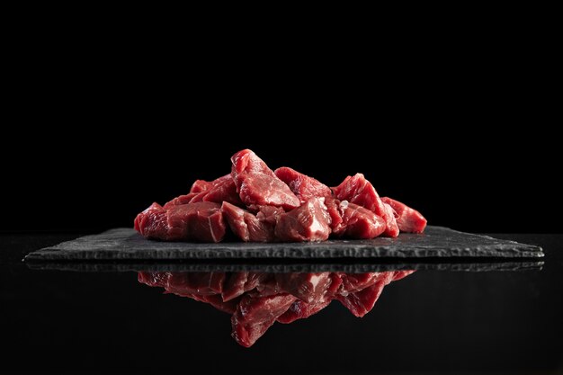 Trozos de carne fresca cruda aislados en negro sobre tablero de piedra vista lateral reflejada